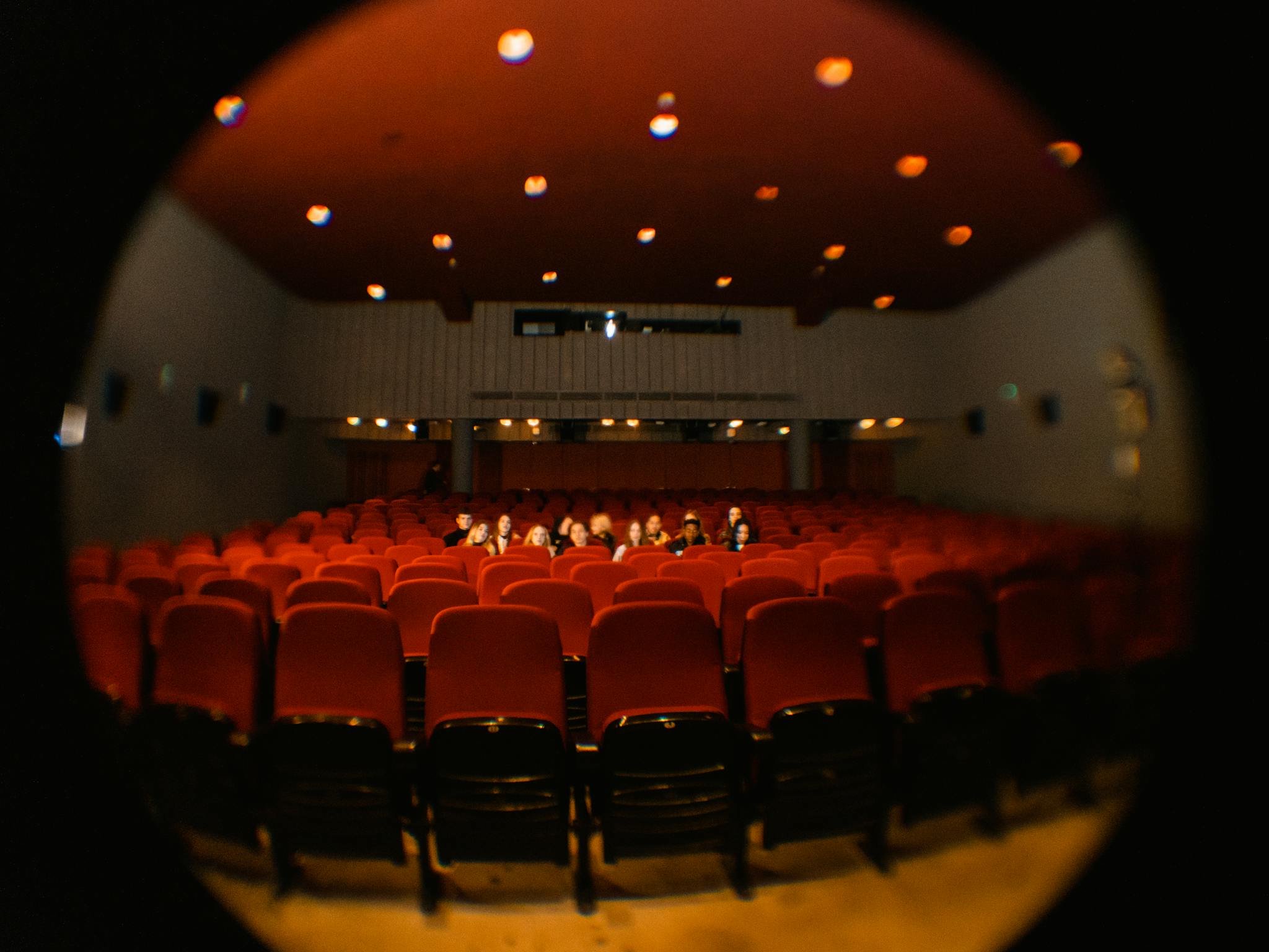 About A fisheye lens captures moviegoers in a dimly lit cinema, offering a unique perspective.