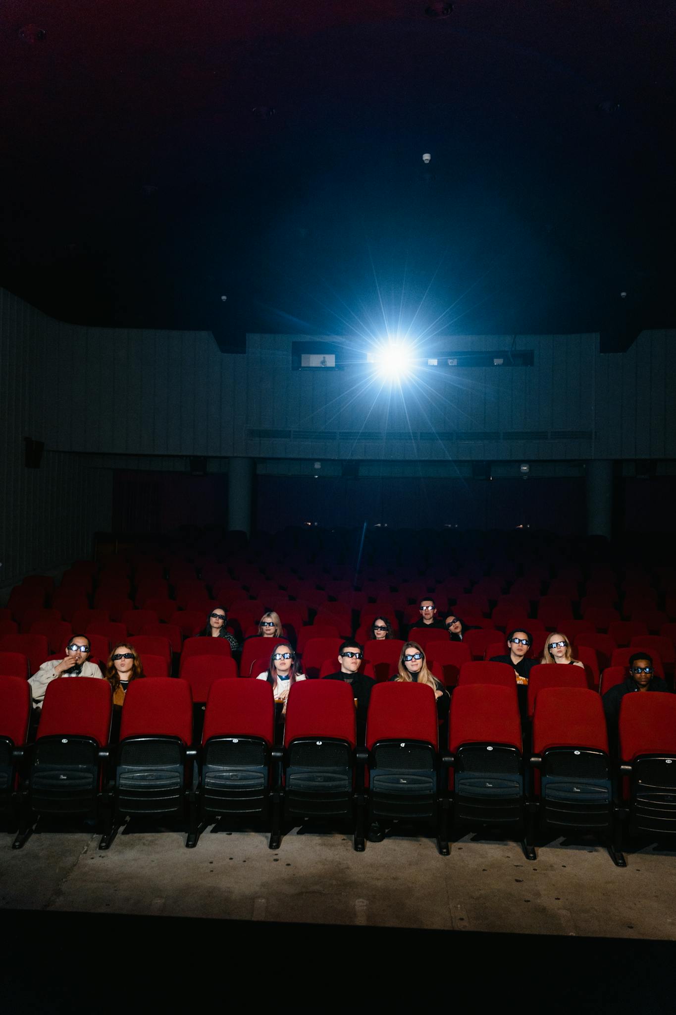 People sitting in a dimly lit movie theater, watching a film with a bright screen.