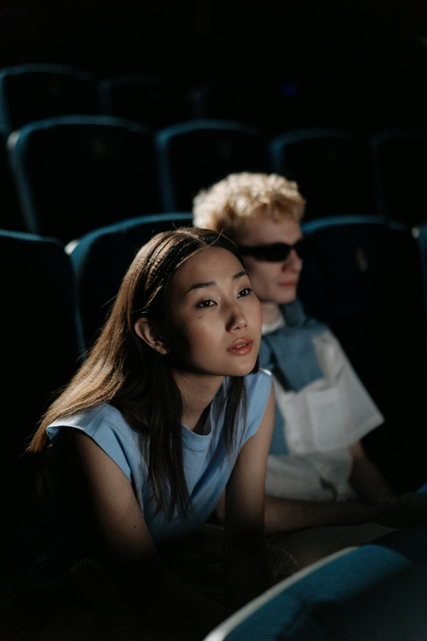 Two young adults watching a movie in a dark theater. Intently focused and immersed.